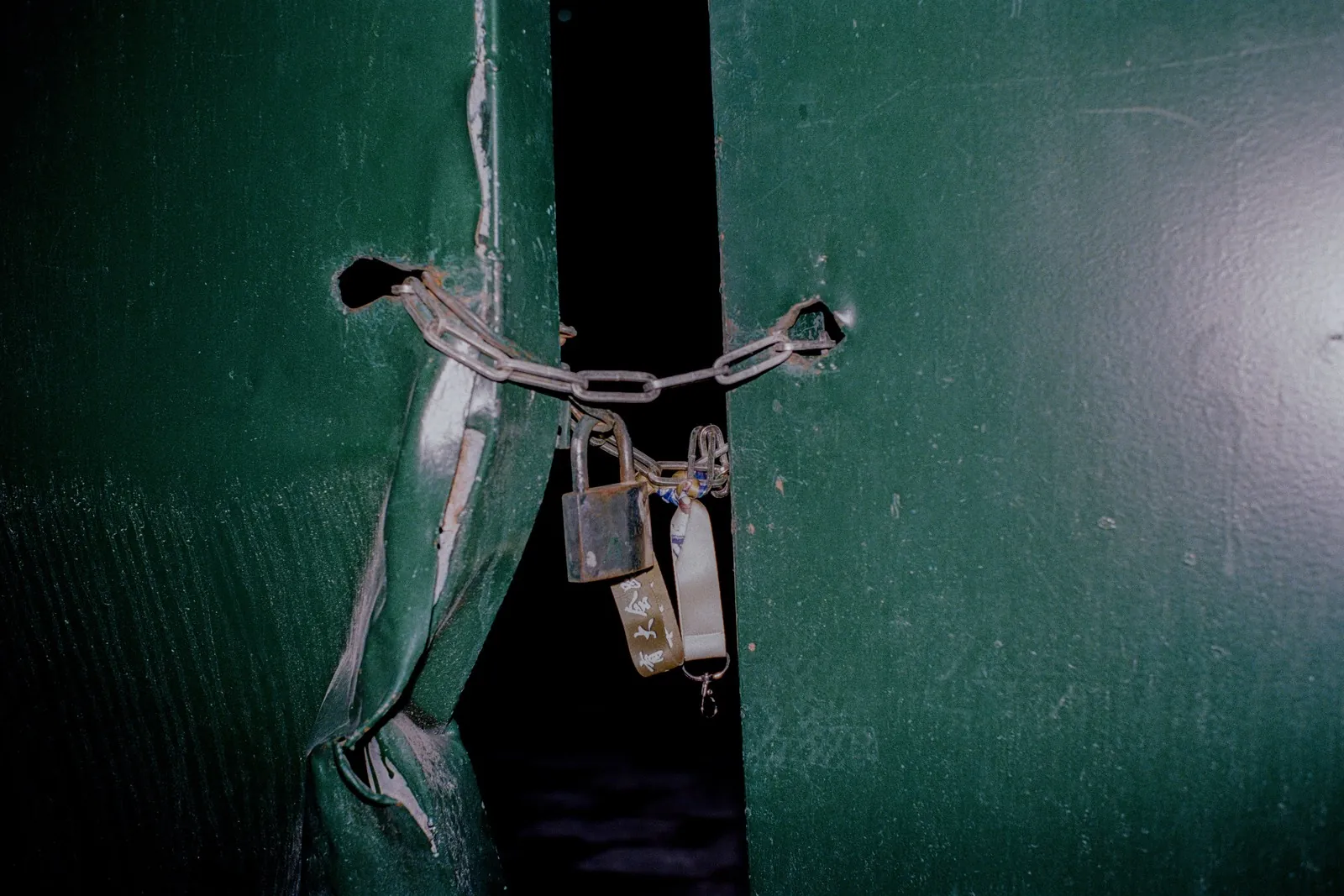 Damaged green door held shut with a chain and padlocks
