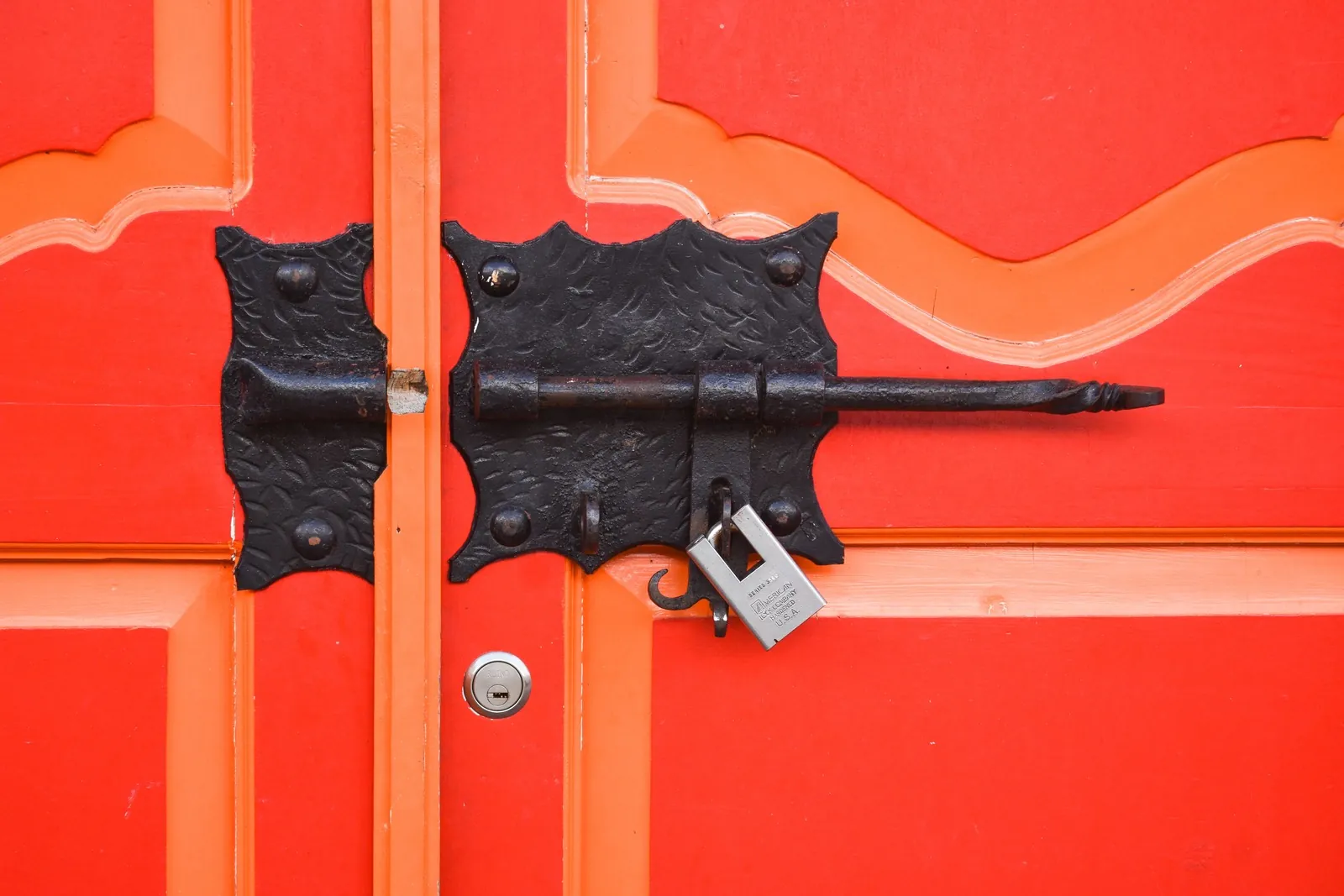 Black iron slide bolt and padlock on a red wooden door
