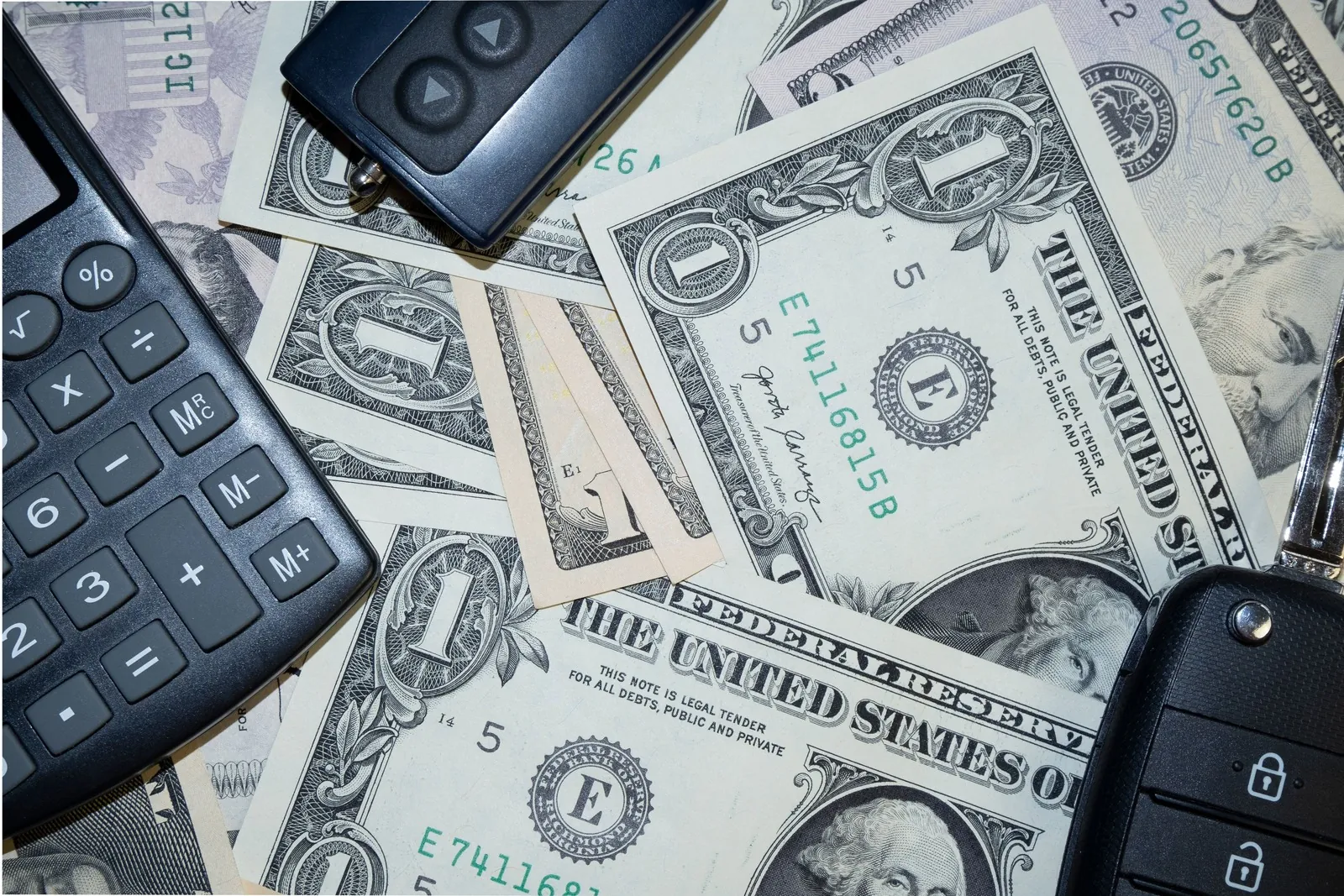 Calculator, dollar bills and a car key fob on a table