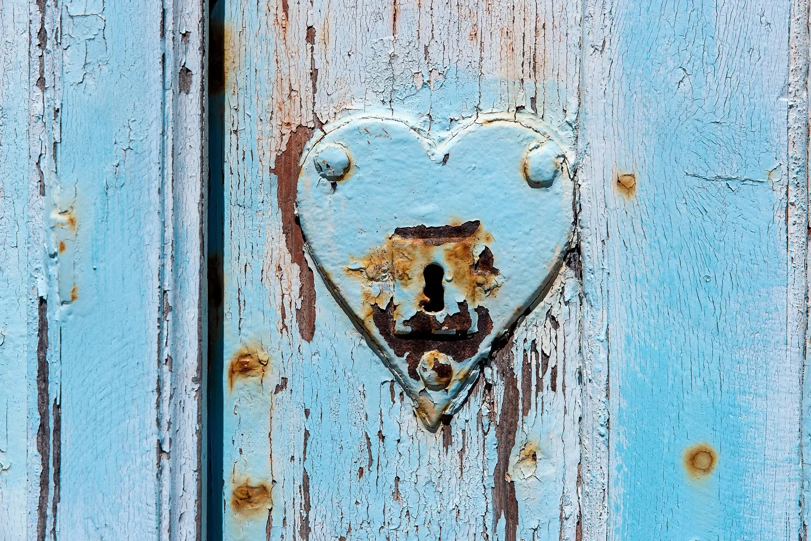 Old keyhole in a heart-shaped plate on a weathered blue door