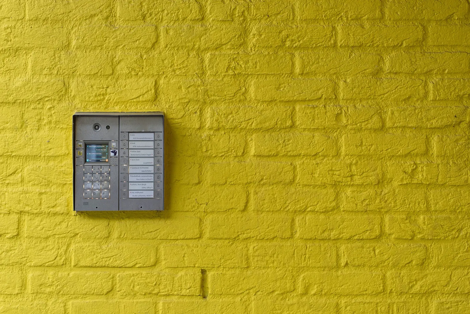 Entry intercom and keypad panel on a yellow brick wall