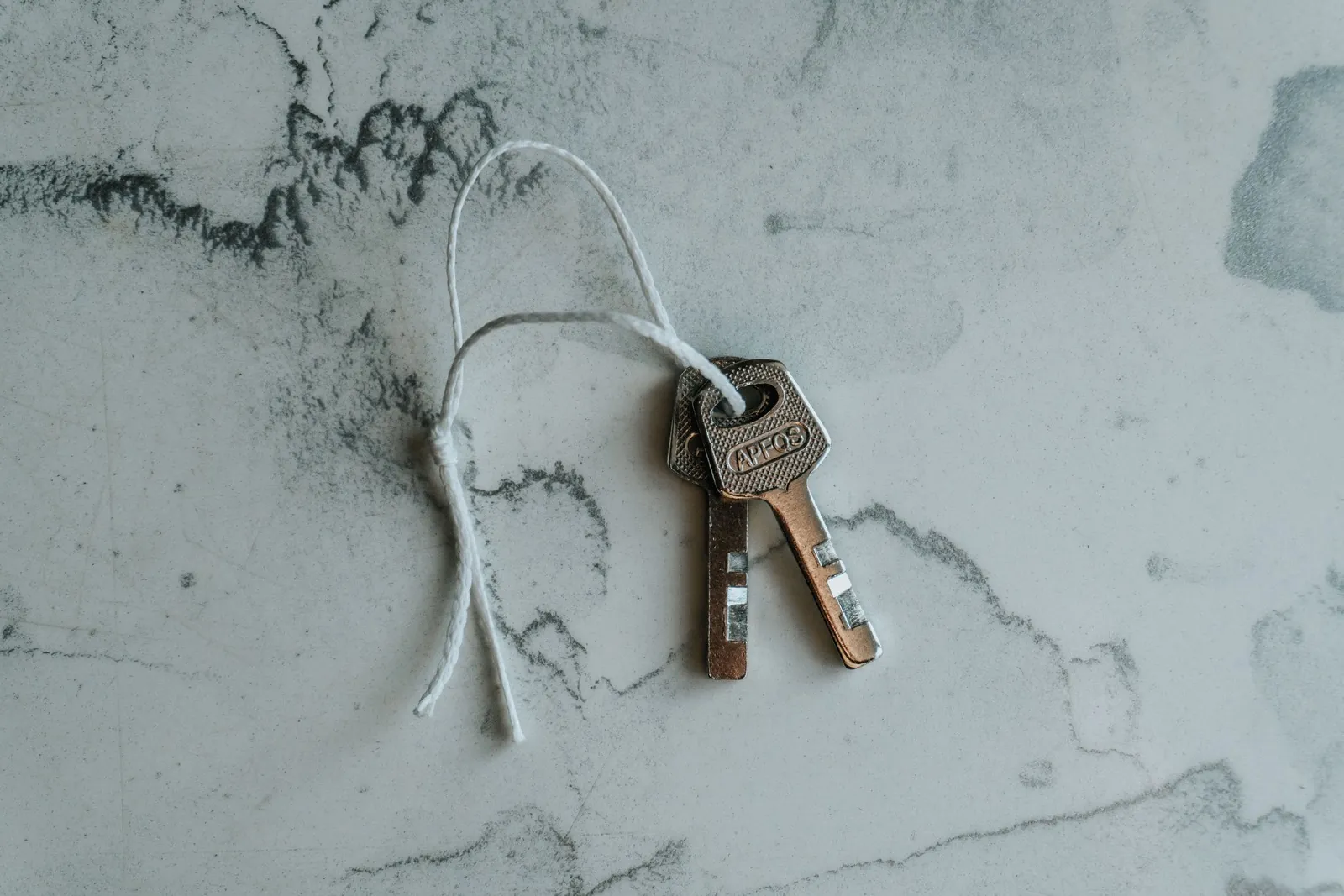 Two house keys on a string lying on a marble surface