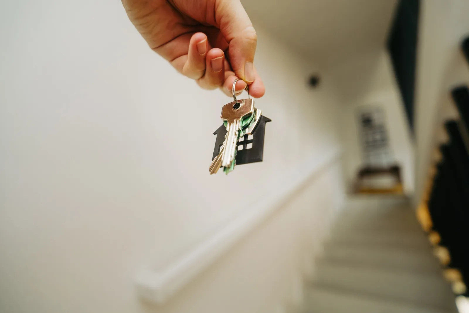 Hand holding a set of house keys on a house-shaped keyring at the top of a staircase