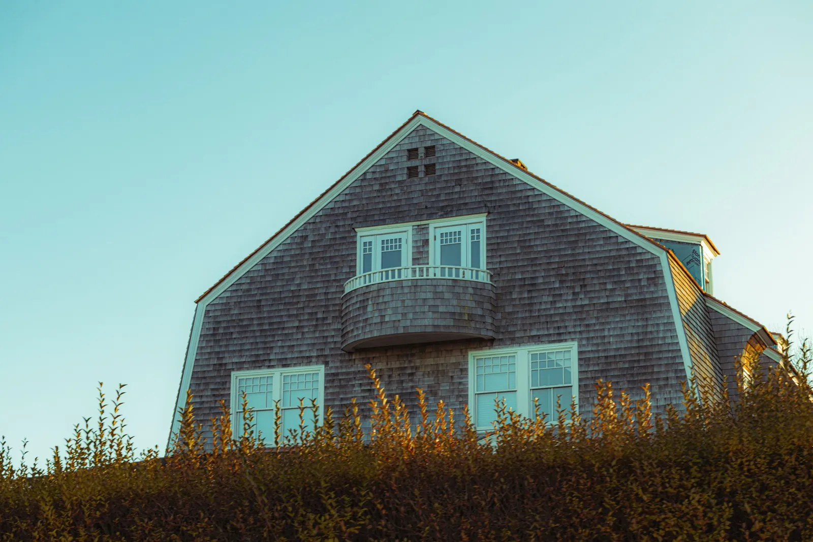 Shingle-sided house with a gambrel roof against a clear sky