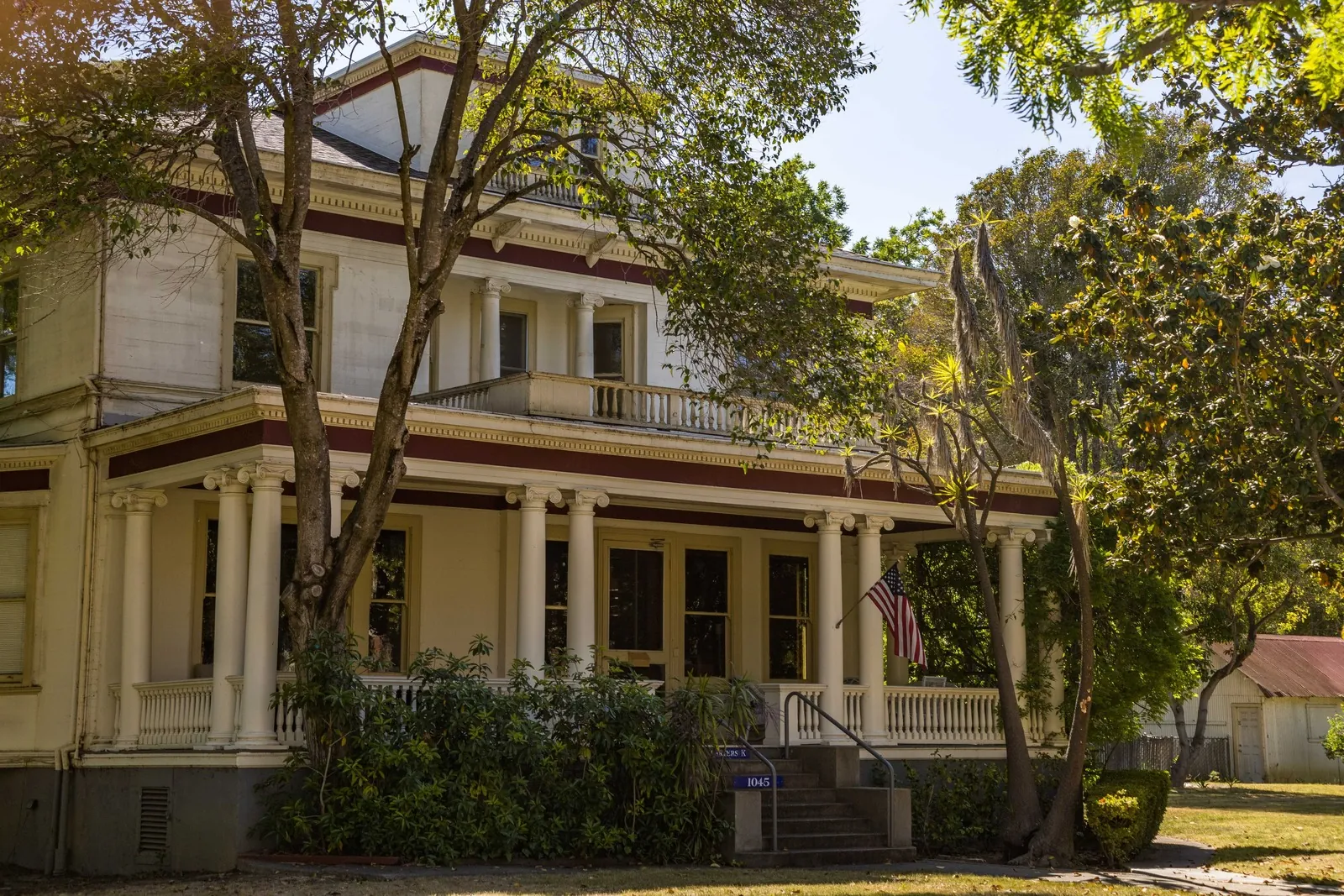 Two-storey house with a wide front porch under tall trees